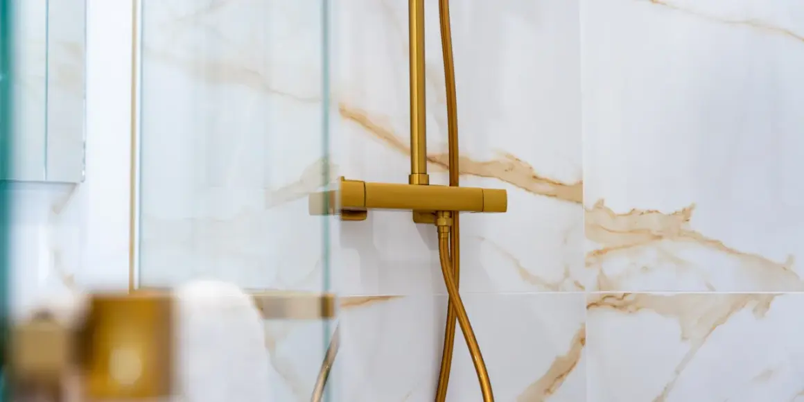 Robinet de douche doré, avec un pommeau réglable en hauteur, sur un mur carrelé de marbre blanc et or.