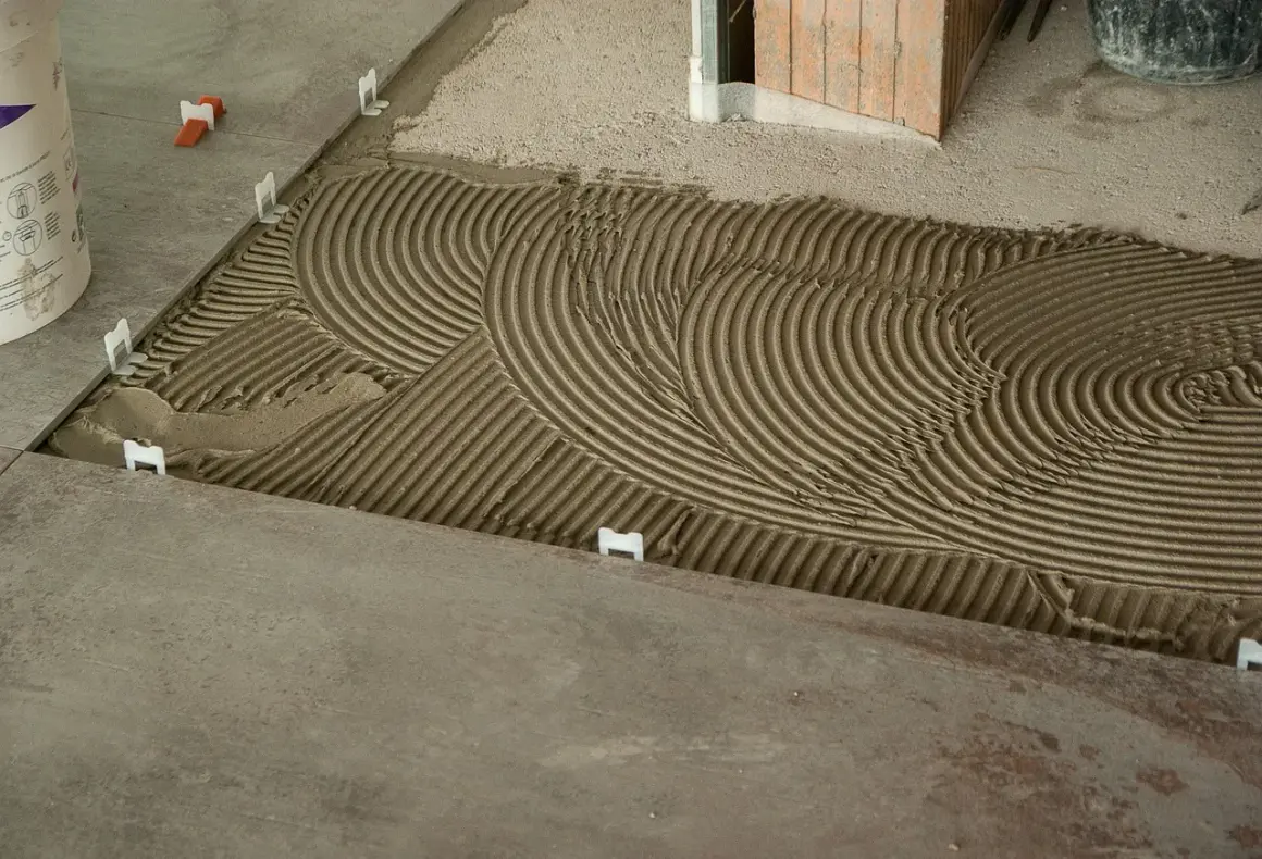 Pose de carrelage : la chape maigre attend les carreaux, avec des croisillons blancs et un lit de colle strié.