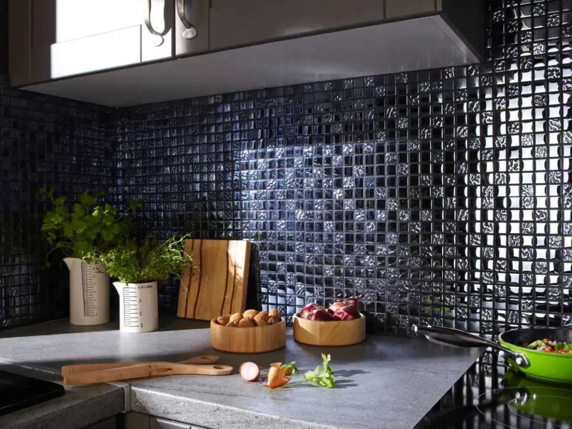 Crédence noire brillante, idéale pour une cuisine moderne. Des herbes fraîches, des oignons et des noix sur le plan de travail. Quelle crédence choisir pour un style audacieux ?