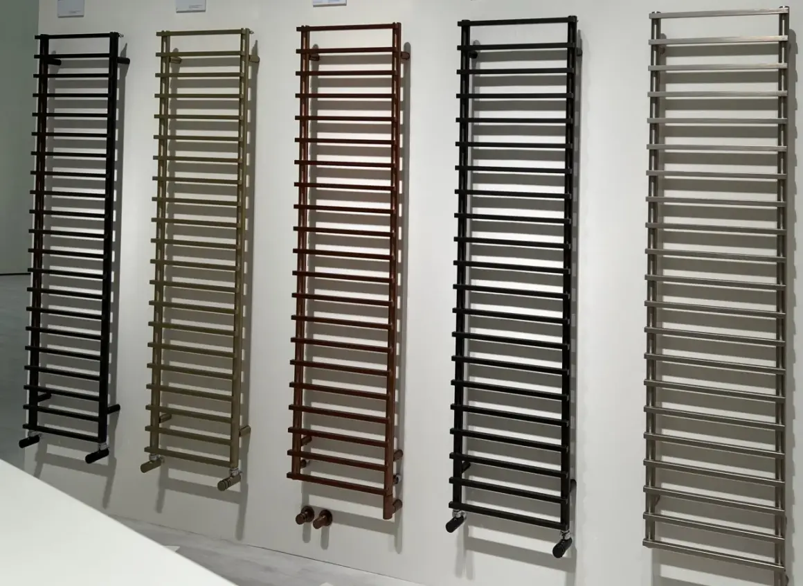 Cinq sèche-serviettes de différentes couleurs (noir, bronze, marron, noir, gris) sont alignés. La hauteur de ces sèche-serviettes est impressionnante.