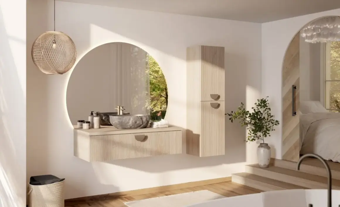 Une salle de bain moderne et chic avec un lavabo en pierre, un miroir rond lumineux et une armoire en bois clair. La lumière naturelle filtre à travers une fenêtre circulaire.