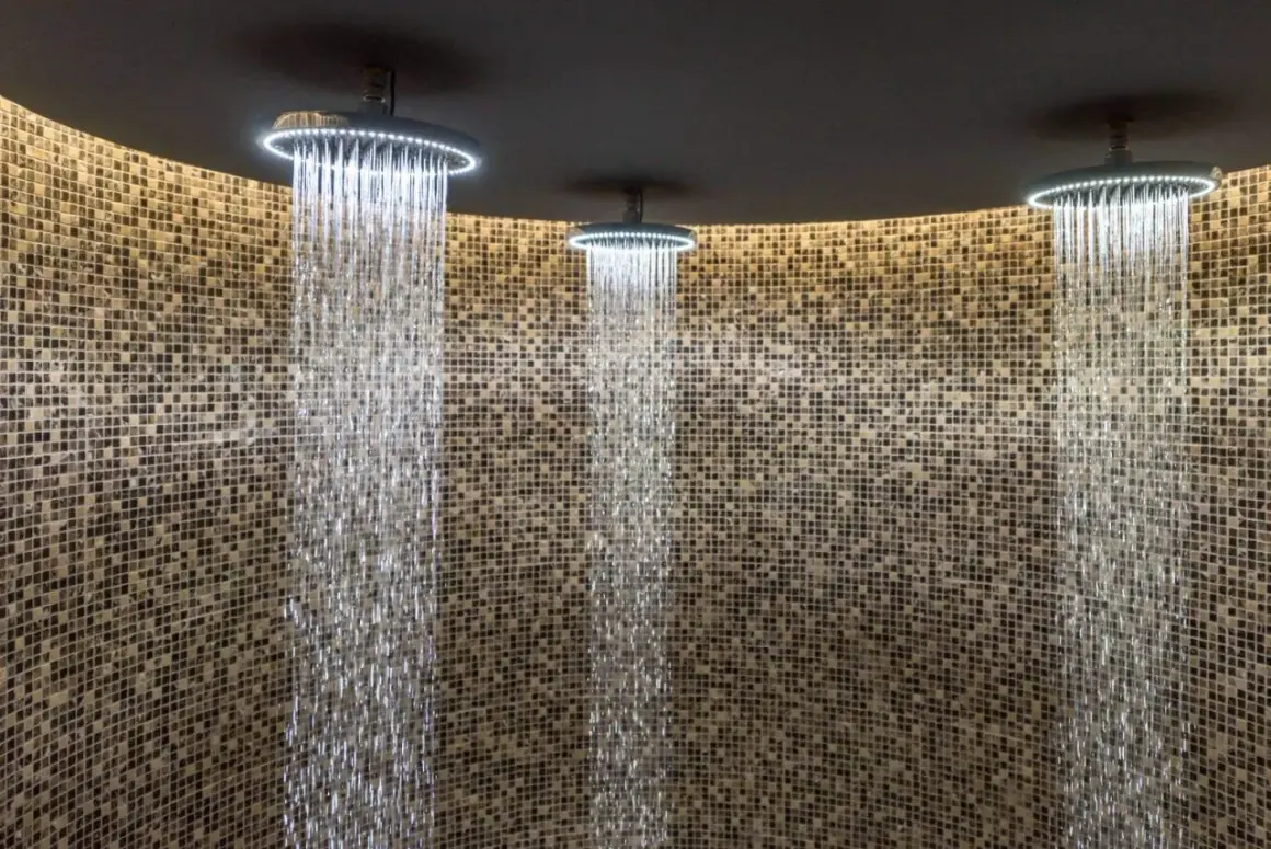 Trois douches modernes avec éclairage LED diffusent des cascades d'eau sur un mur de mosaïque. Une expérience de douche sensorielle unique.