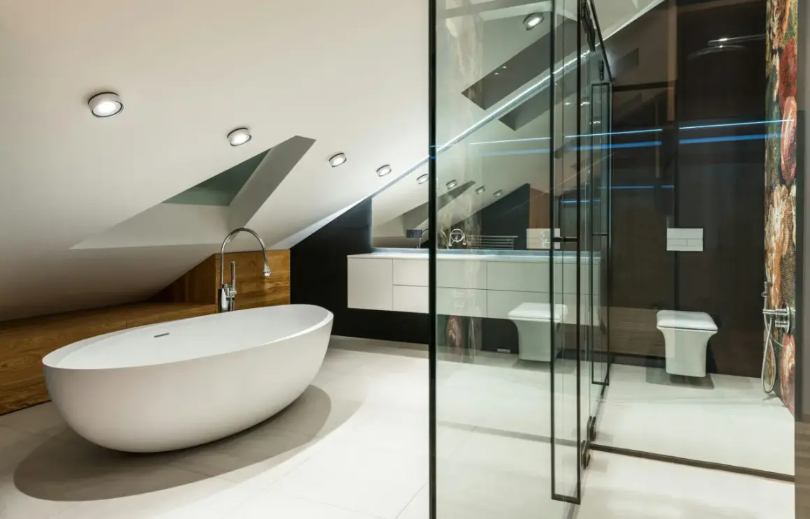 Élégante petite salle de bain mansardée avec baignoire îlot, douche vitrée, lavabo suspendu et WC.