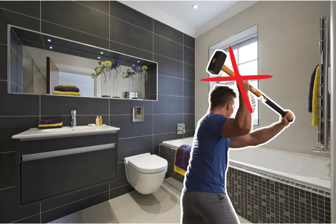 Un homme s'apprête à démolir une salle de bain moderne avec une masse. Une croix rouge indique que cette méthode n'est pas recommandée pour la renovation carrelage.