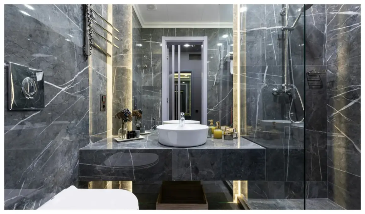 Une **salle de bain de rêve** aux murs de marbre gris, avec vasque ronde, douche moderne et éclairage d'ambiance.