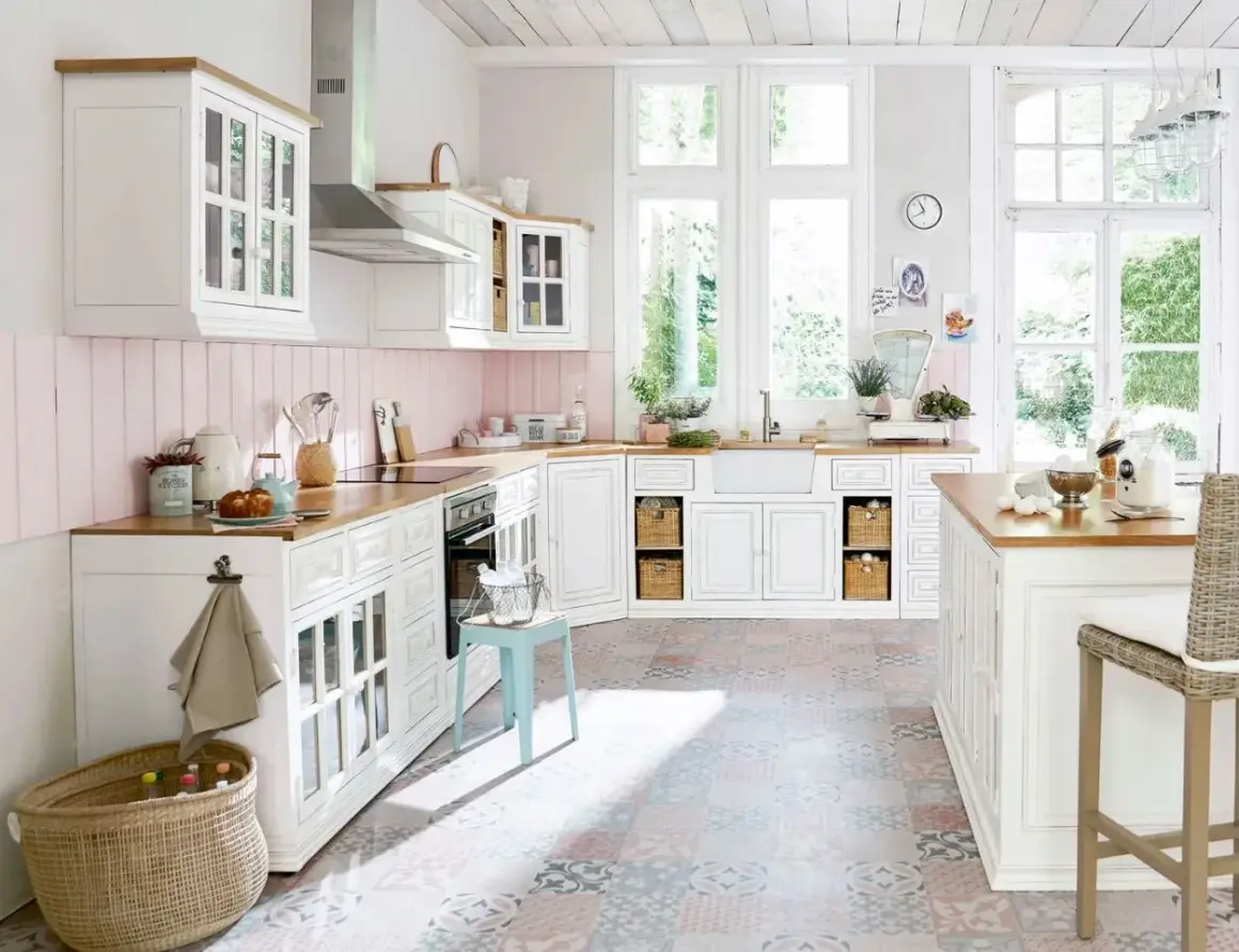 Une cuisine campagne chic lumineuse avec des meubles blancs, un plan de travail en bois, un carrelage coloré et de grandes fenêtres donnant sur le jardin.