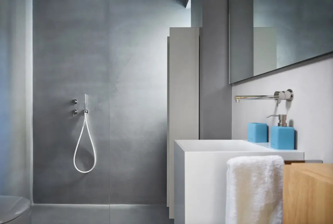 Salle de bain moderne avec douche sans carrelage, lavabo blanc et accessoires bleus.