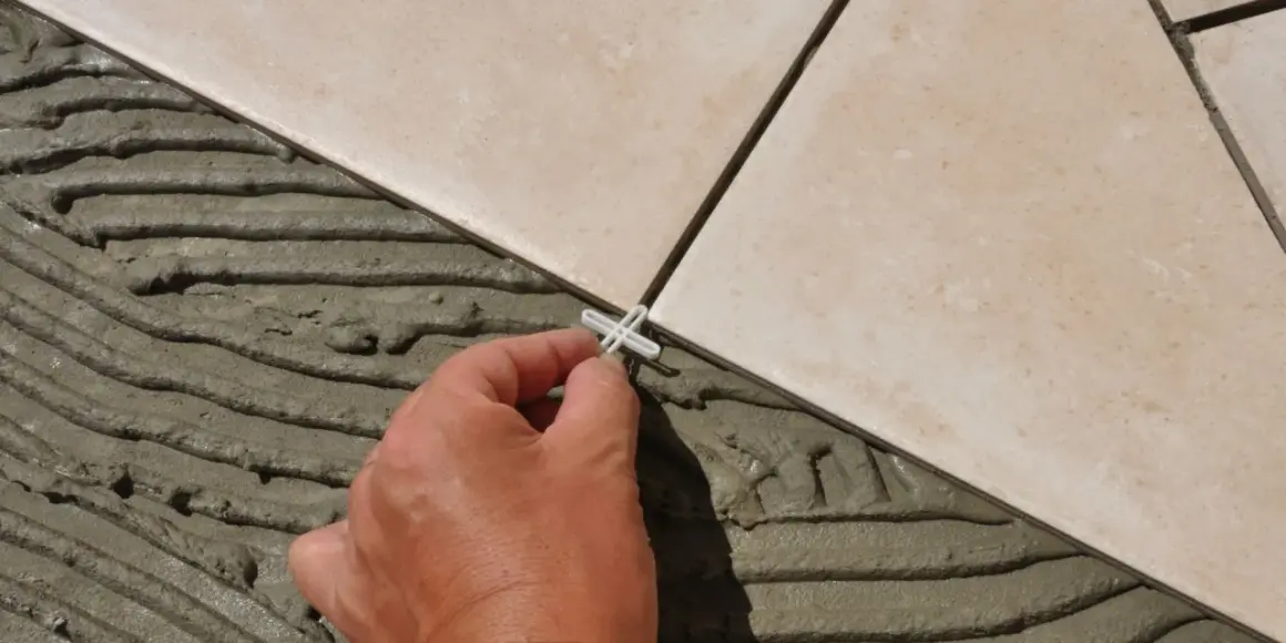 Pose de carrelage en cours, une main place un croisillon. Le prix pose carrelage m2 dépend de la complexité.