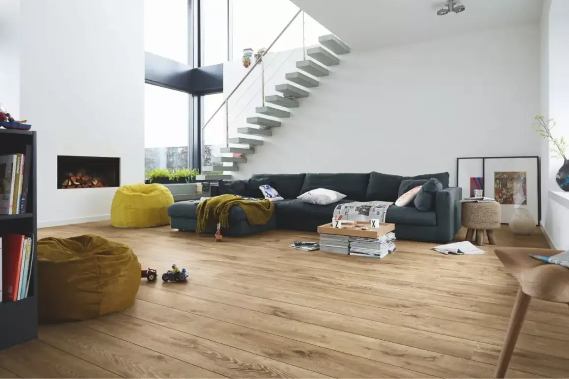 Salon moderne avec canapé, cheminée, poufs et escalier flottant. Le parquet flottant, d'une épaisseur idéale, réchauffe l'espace.