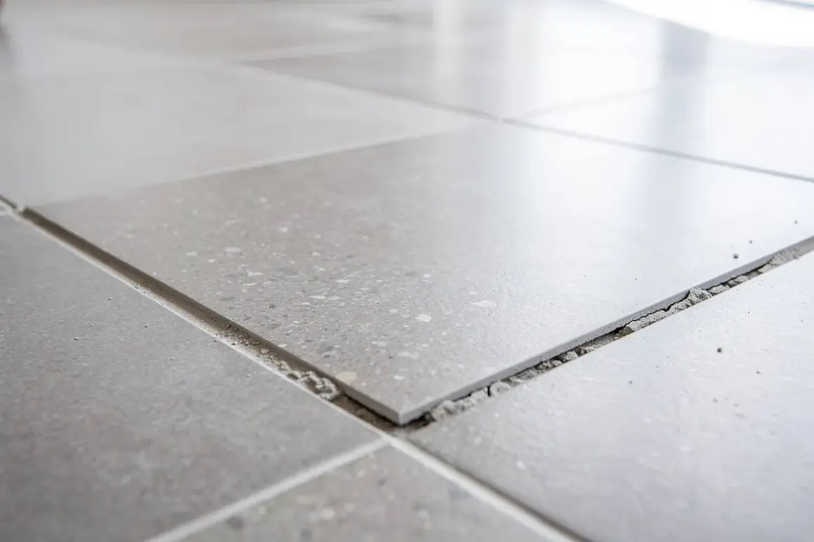 Carrelage gris, certaines dalles se soulèvent, révélant le gravier en dessous. Un signe de vieillissement, peut-être une décennale carrelage à prévoir.