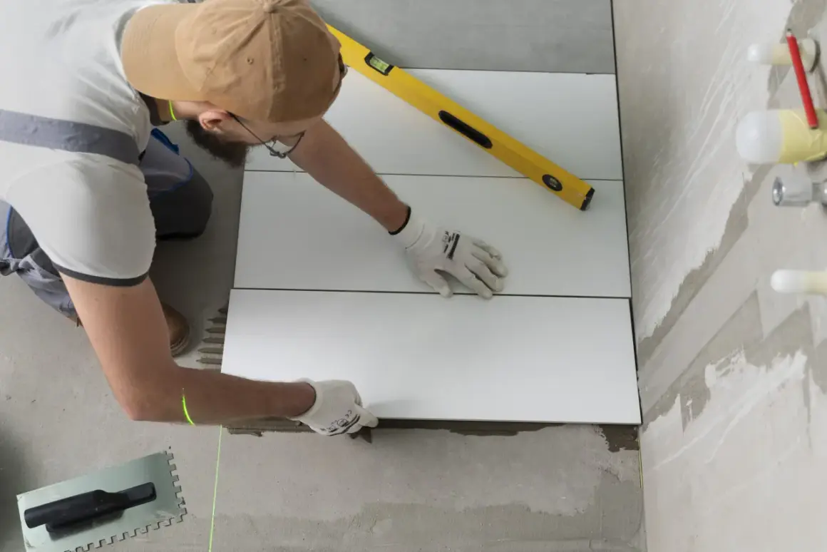 Pose d'un carrelage mural de salle de bain. Un carreleur utilise un niveau et un laser pour un calcul précis.