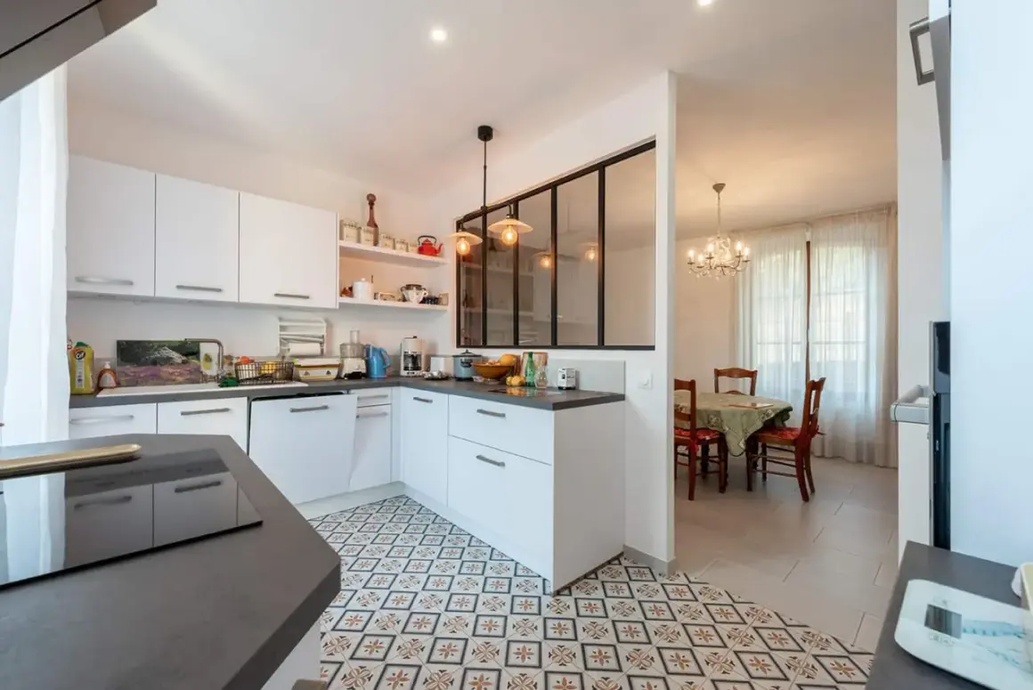 Carrelage décoratif au sol pour la délimitation carrelage cuisine salon. Une cuisine moderne blanche ouverte sur une salle à manger avec lustre.