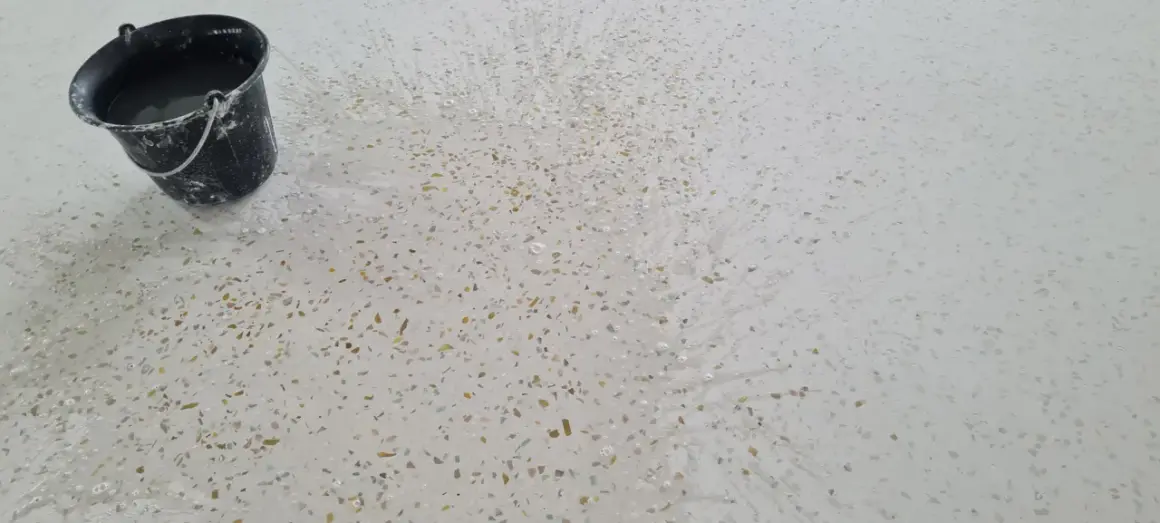 Un seau d'eau éclabousse un sol en terrazzo blanc moucheté, révélant comment faire briller un sol en terrazzo.
