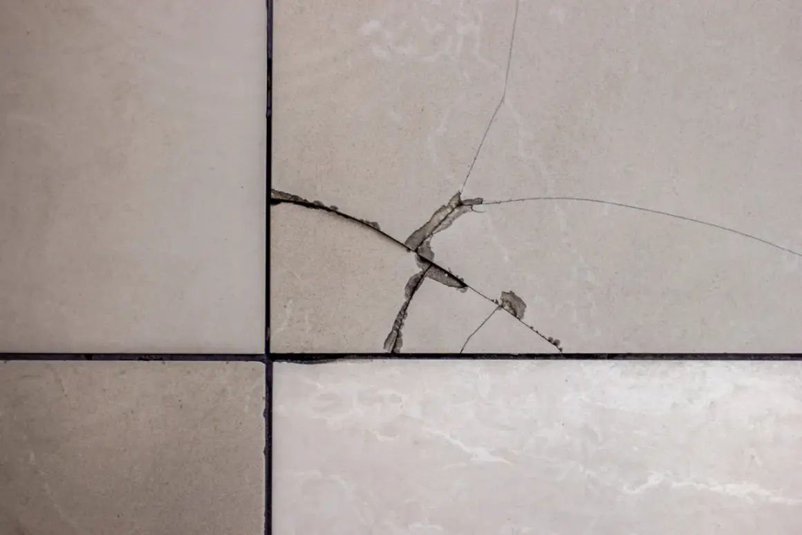 Gros plan sur un carrelage beige fissuré, montrant les étapes pour comment reparer un eclat de carrelage.