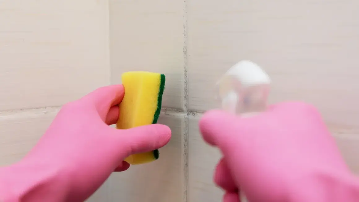 Main rose gantée tient une éponge jaune pour nettoyer une tache sur carrelage qui ne part pas.