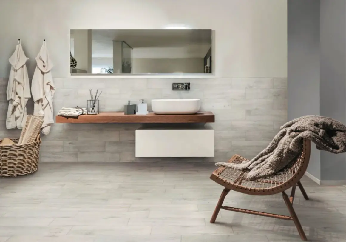 Salle de bain moderne avec murs et sol en grès cérame émaillé effet bois, lavabo suspendu, fauteuil confortable.