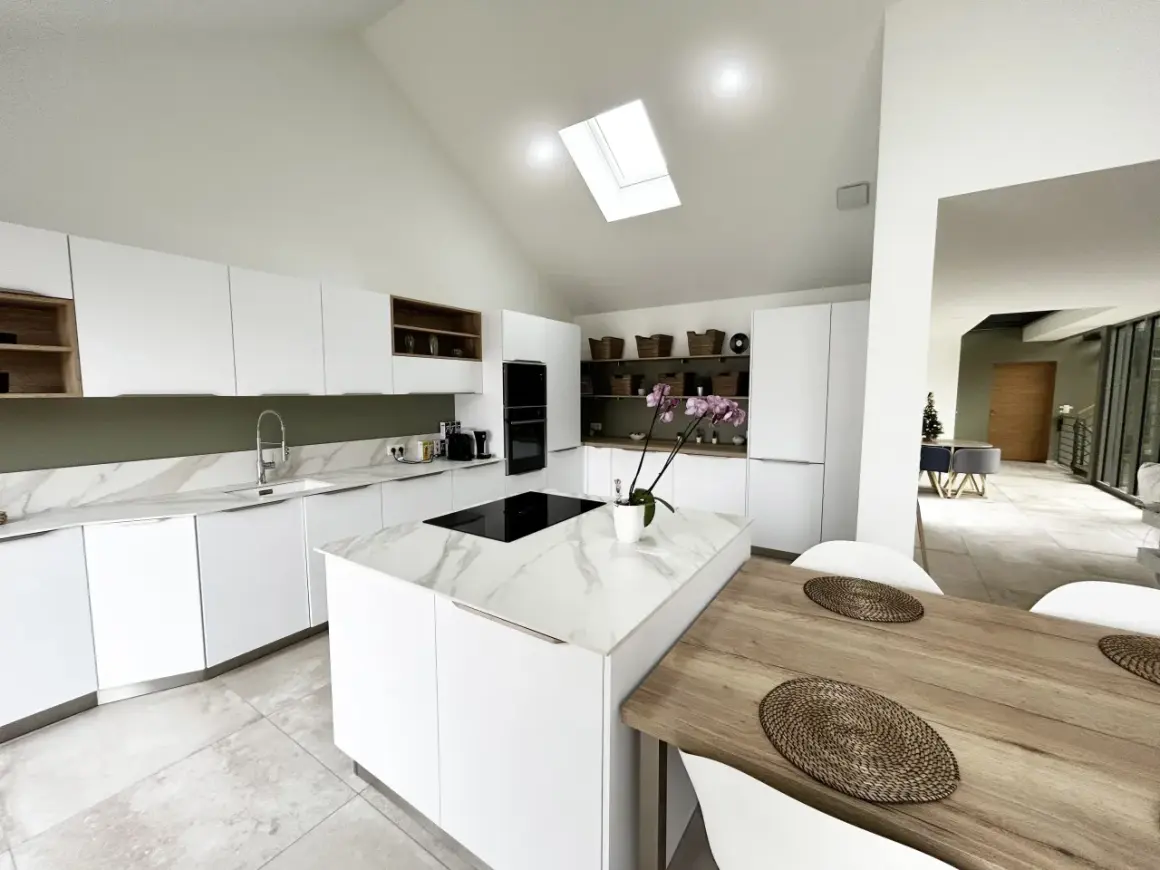 Cuisine moderne avec îlot central en marbre blanc et bois. Éclairage naturel par puits de lumière.