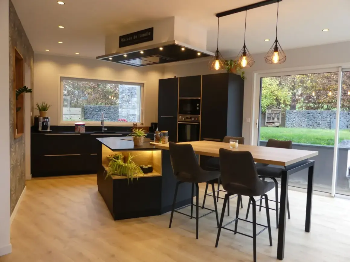 Cuisine moderne avec îlot central, plan de travail noir et carrelage marron foncé. Table haute avec tabourets, luminaire design.
