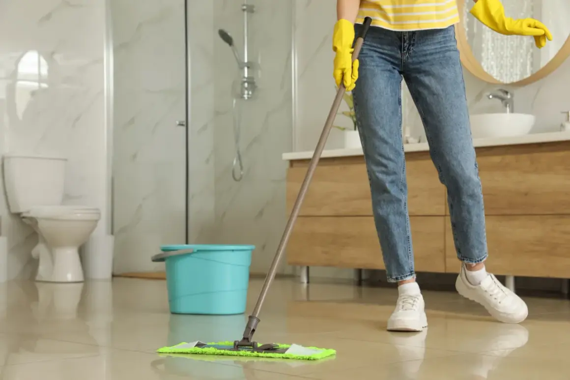Nettoyer carrelage après chantier : une personne en gants jaunes passe la serpillière sur un sol brillant dans une salle de bain moderne.