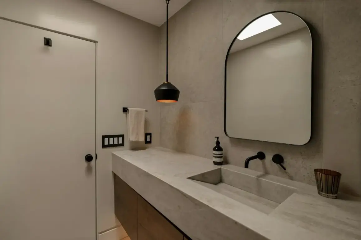 Élégante salle de bain avec un lavabo en **béton ciré** intégré, un miroir arqué et un éclairage moderne.