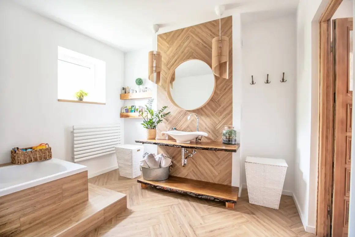 Salle de bain moderne avec sol et murs en bois, baignoire, lavabo et miroir. On peut mettre du parquet dans une salle de bain si le matériau est adapté.