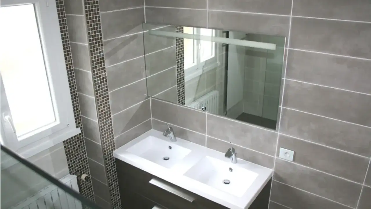 Salle de bain moderne avec double vasque, miroir, fenêtre et carrelage sur placo gris et mosaïque.