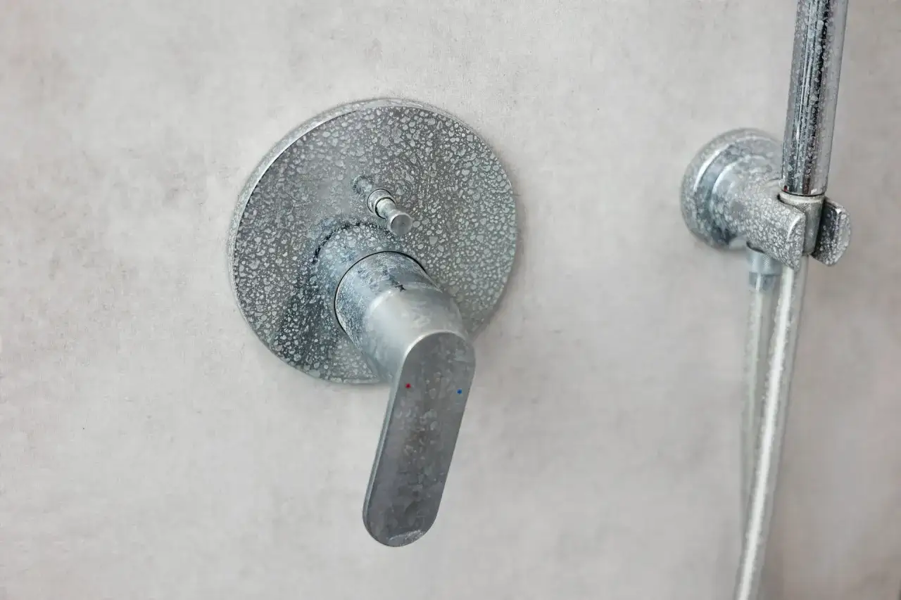 Robinet de douche avec traces de calcaire, t&eacute;moignant de l'usure dans cette salle de bain.