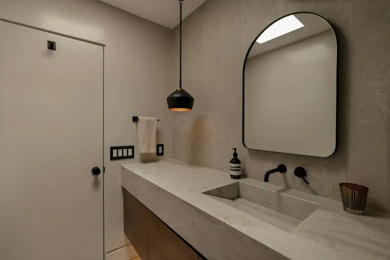 Élégante salle de bain avec un lavabo intégré en béton ciré, un miroir arqué et une suspension moderne.