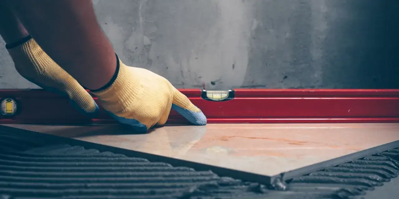 Pose d'un carrelage avec un niveau à bulle pour vérifier l'épaisseur et la planéité.