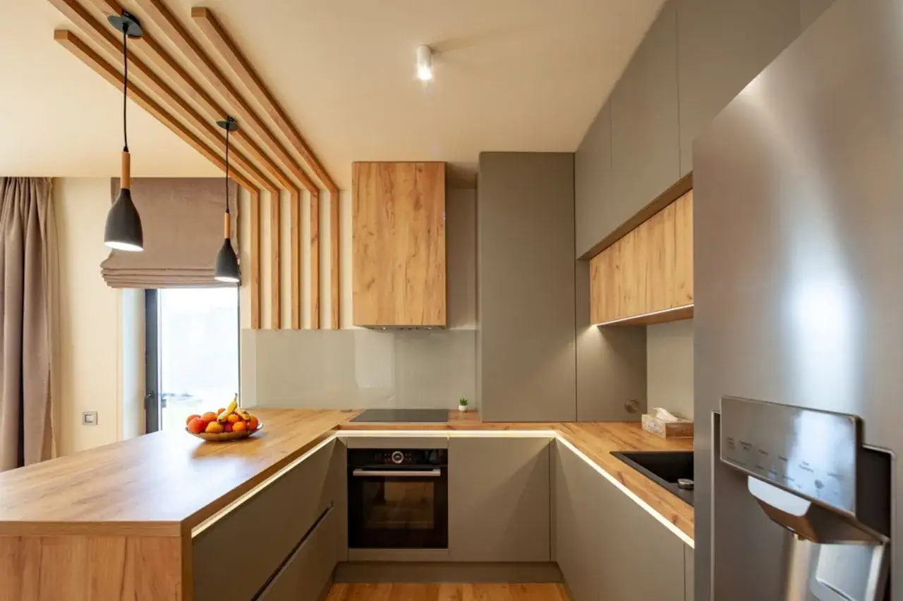 Cuisine moderne avec plan de travail en bois, idéal pour recouvrir un plan de travail carrelé. Évier noir, four encastré, réfrigérateur argenté.
