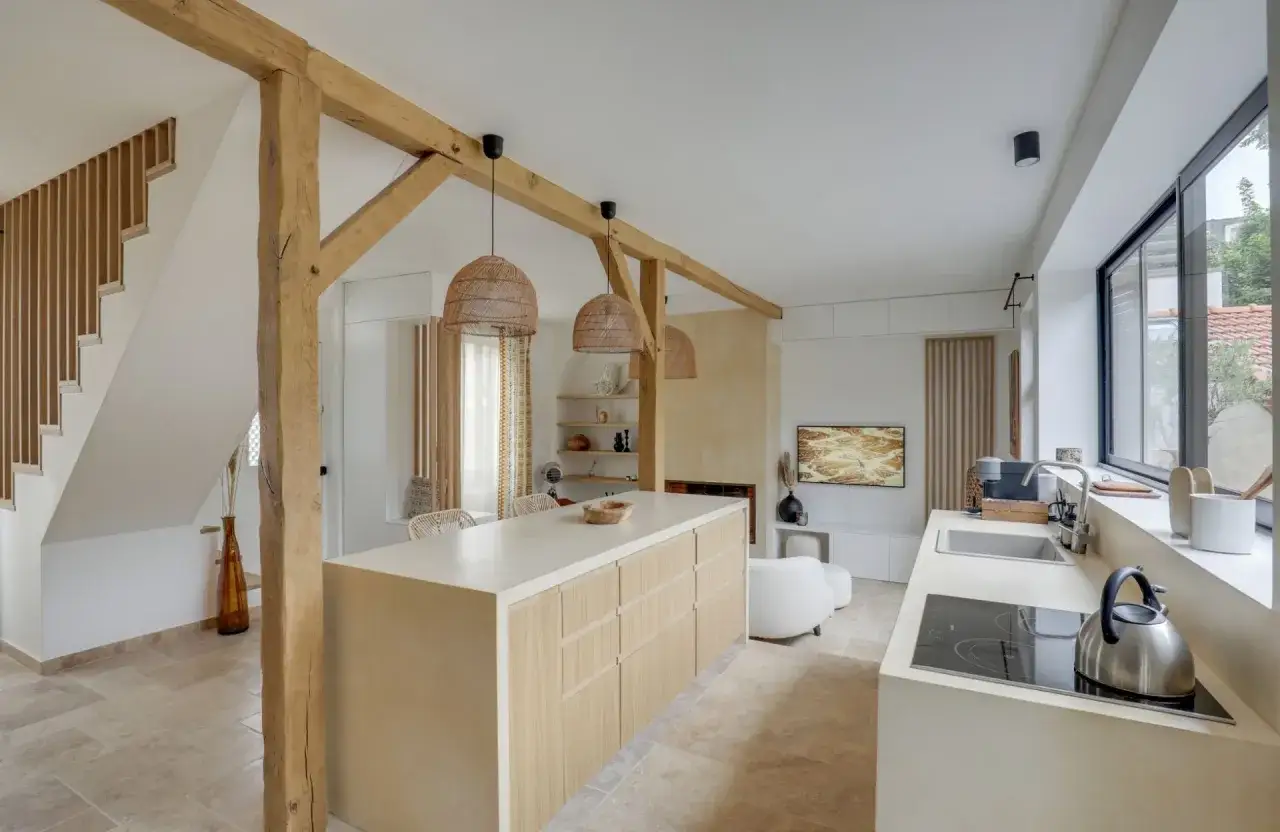 Plan d'une cuisine en longueur avec îlot central en bois clair, poutres apparentes, et un coin salon TV.