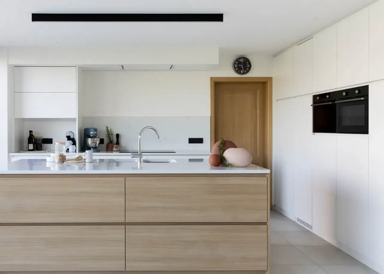 Îlot central en bois clair, plan de travail en marbre, électroménager intégré. Une touche de deco cuisine moderne avec des vases et des herbes aromatiques.