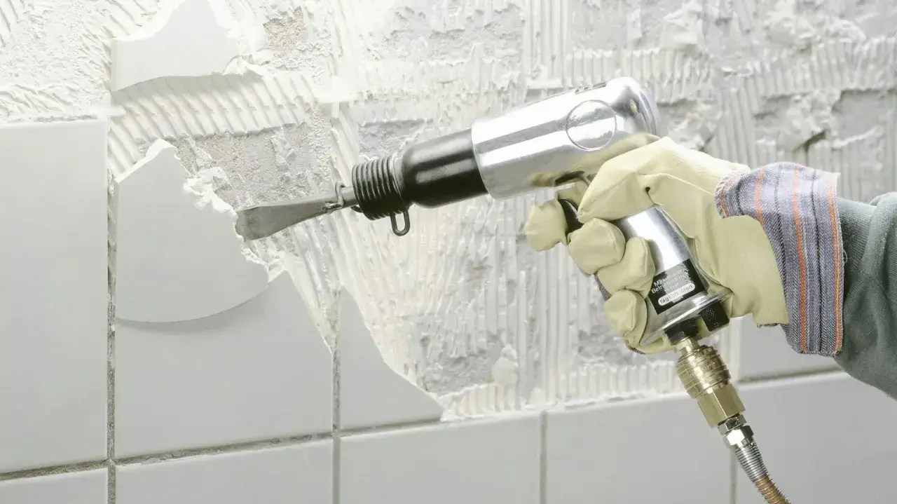 Main pneumatique en action pour enlever carrelage mural. Le burin attaque le mur, brisant les carreaux blancs.