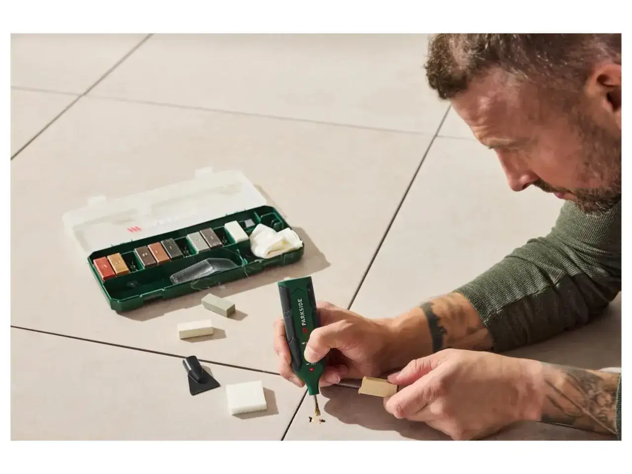 Un homme répare un carrelage rayé avec un kit de réparation.