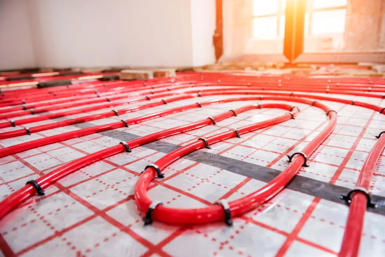 Installation de tubes rouges pour plancher chauffant, prêts à être recouverts de colle et de carrelage pour un confort optimal.