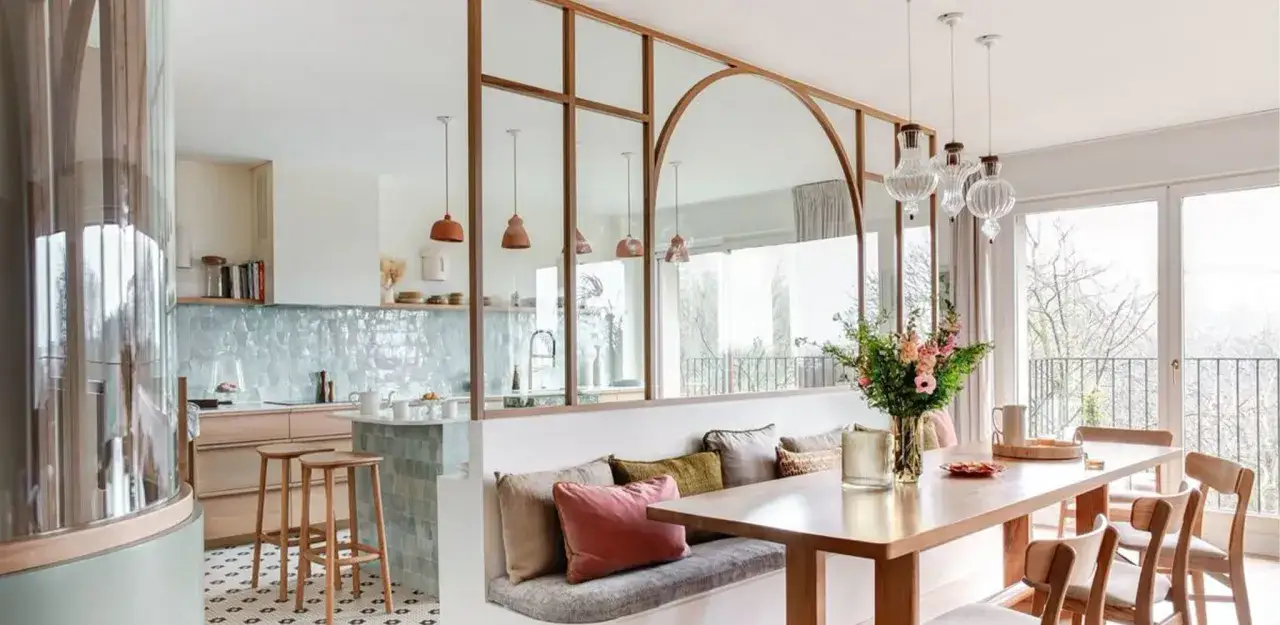 Un élégant modèle de cuisine ouverte avec un îlot central, des banquettes confortables et une table à manger, séparés par une verrière stylisée.