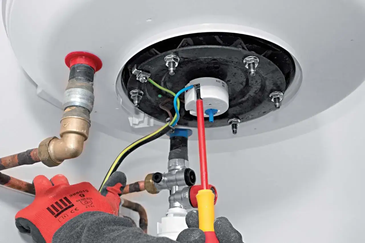 Mains &eacute;lectriques et tuyauterie en cuivre pour changer un ballon d'eau chaude. Un tournevis est utilis&eacute; pour les connexions.
