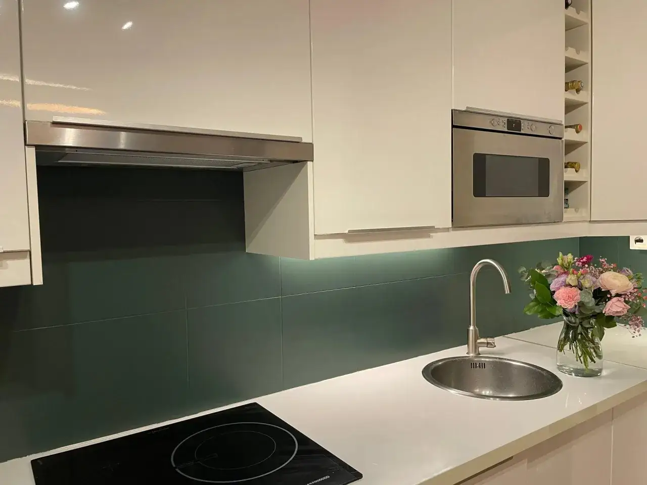 Cuisine moderne avec crédence vert foncé. Quelle peinture pour carrelage mural cuisine ? Un bouquet de fleurs décore le plan de travail près de l'évier.