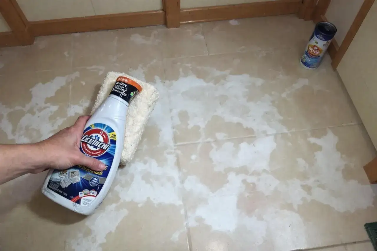 Main d'une personne tenant un flacon de produit nettoyant et une éponge pour comment nettoyer un carrelage neuf.