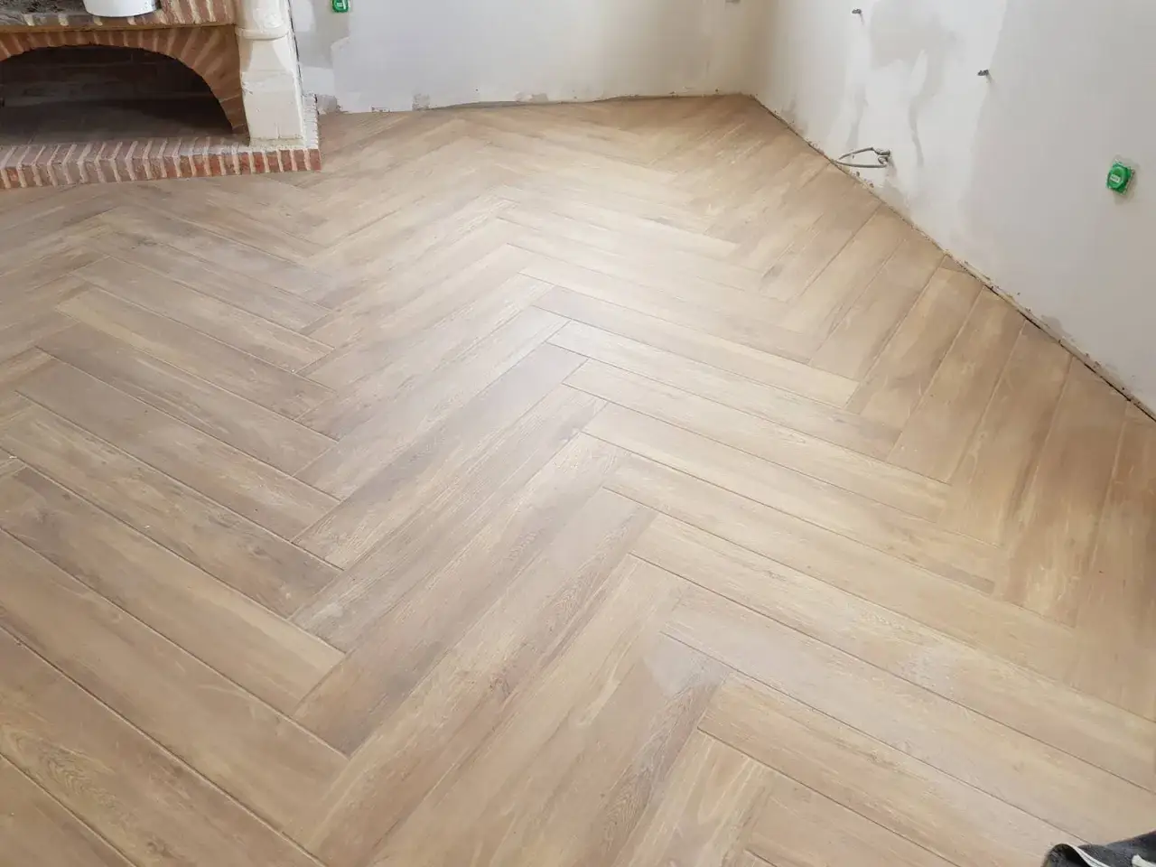 Un sol en bois clair, posé en chevron, apporte une touche chaleureuse à cette pièce en cours d'aménagement, près d'une cheminée en briques.