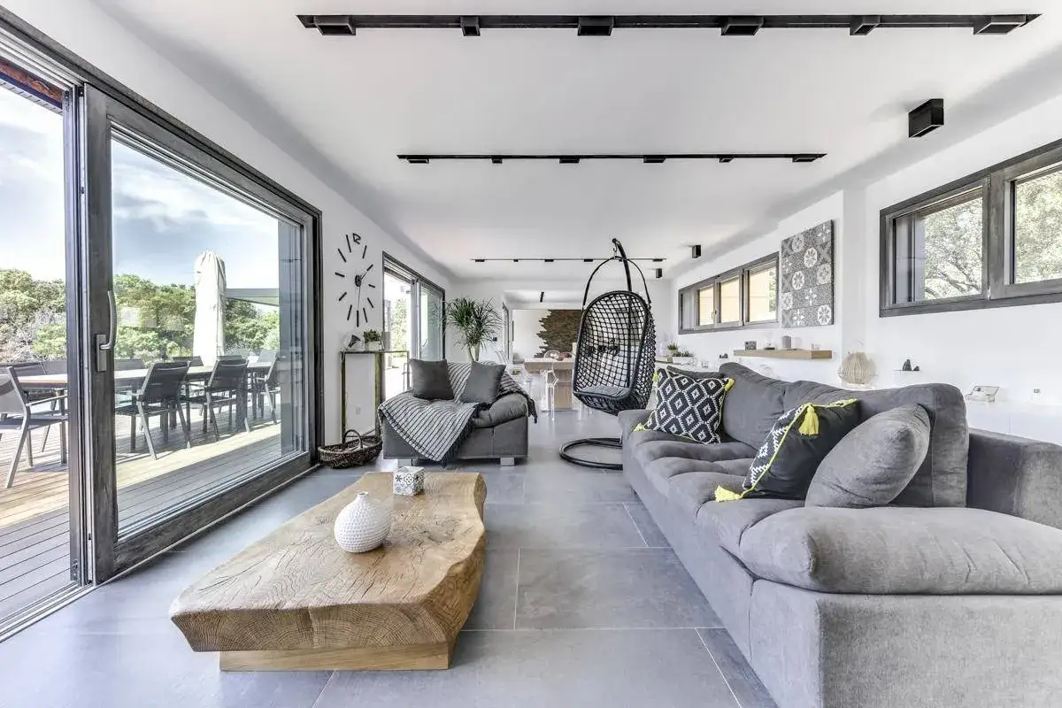 Salon moderne avec grand canapé gris, fauteuil suspendu, table basse en bois brut et carrelage au sol. Idéal pour choisir carrelage.