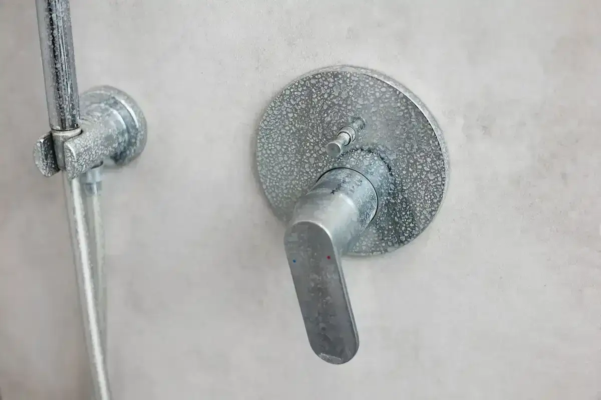 Mitigeur de douche entartr&eacute;, pr&ecirc;t &agrave; changer pour un nouveau. Le pommeau de douche est aussi visible.