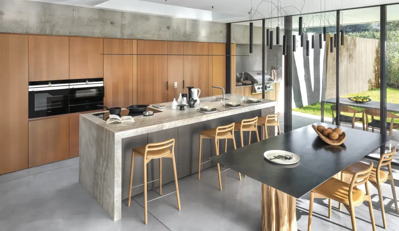 Cuisine moderne avec &icirc;lot central en marbre, tabourets en bois et vue sur jardin. Une belle cuisine inspiration pour vos repas.