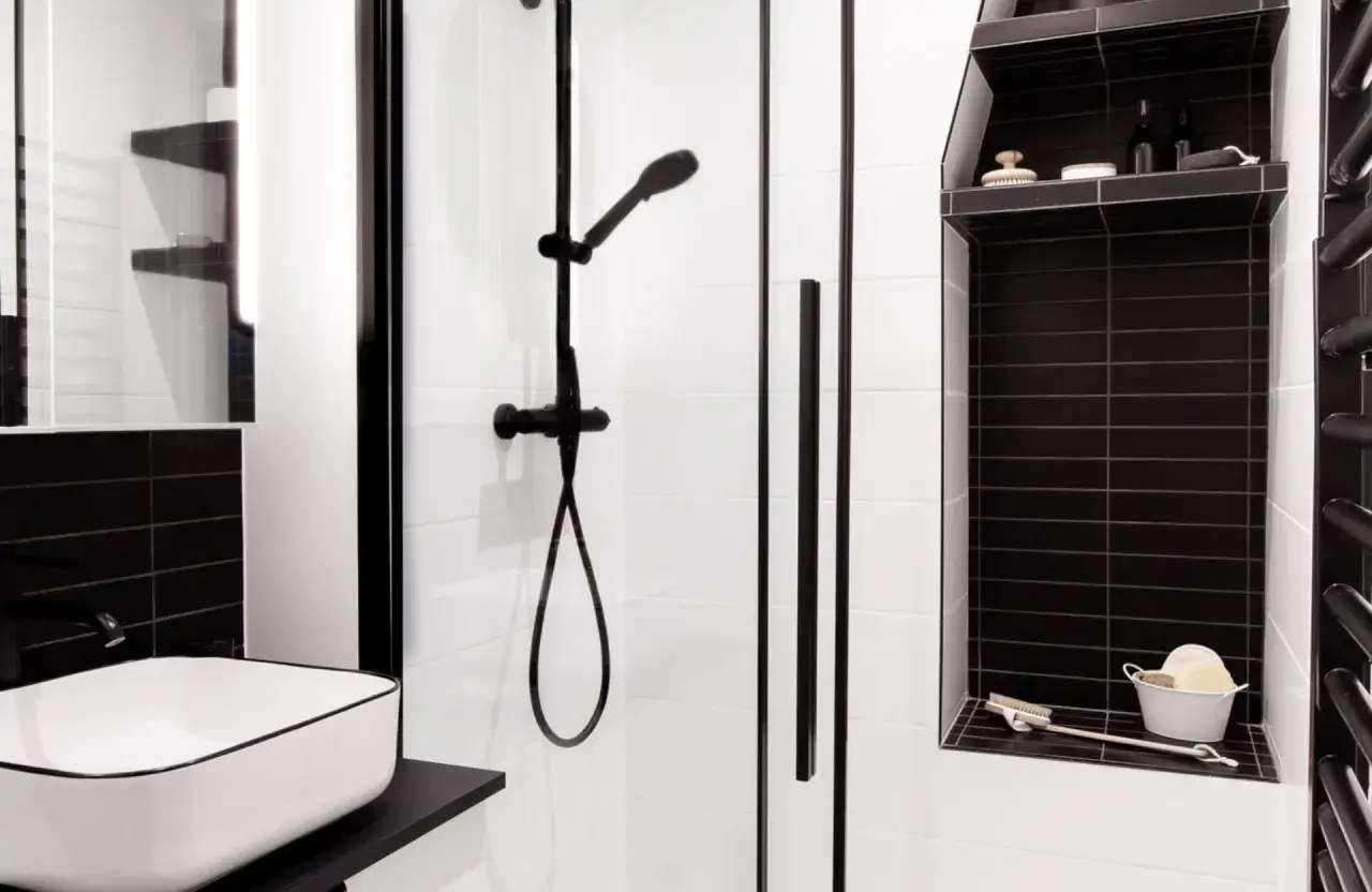 Salle de bain beige et noir avec douche moderne, lavabo design et étagères murales.