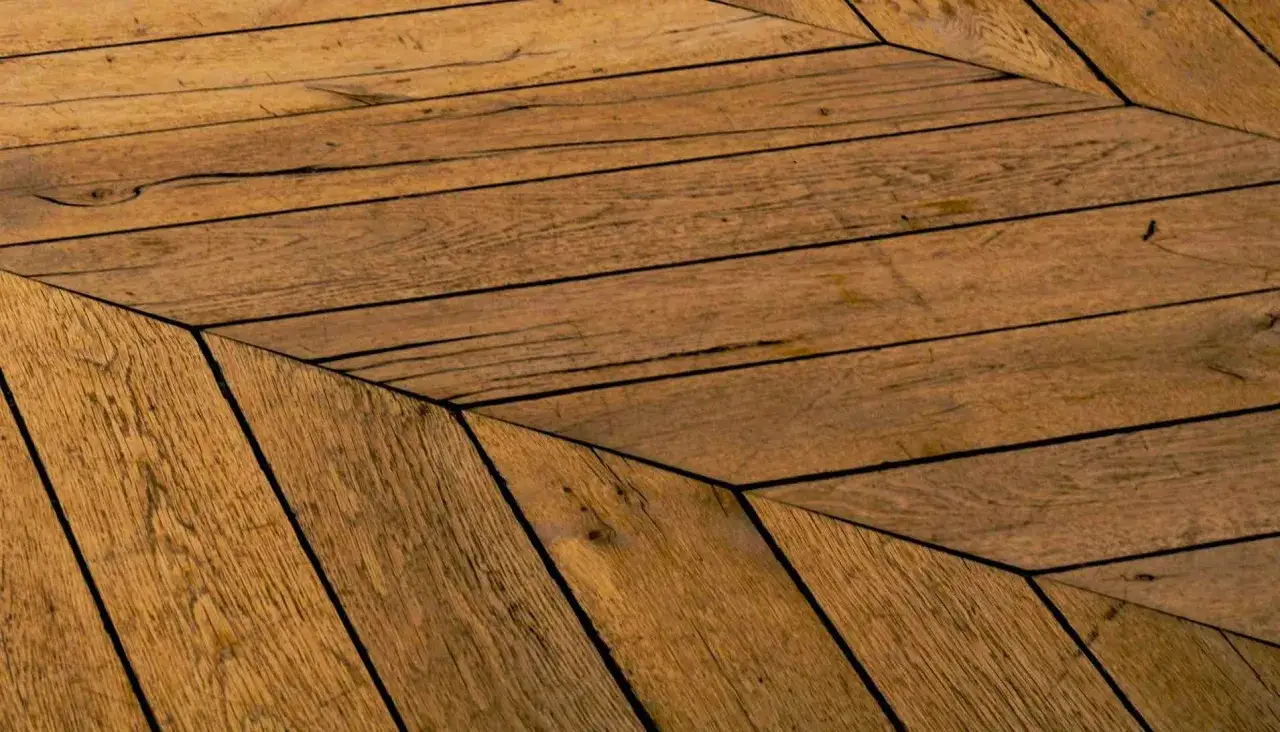 Gros plan sur un type de parquet en bois vieilli, posé en chevrons. Les lames présentent des craquelures et des nœuds, témoignant de leur âge.