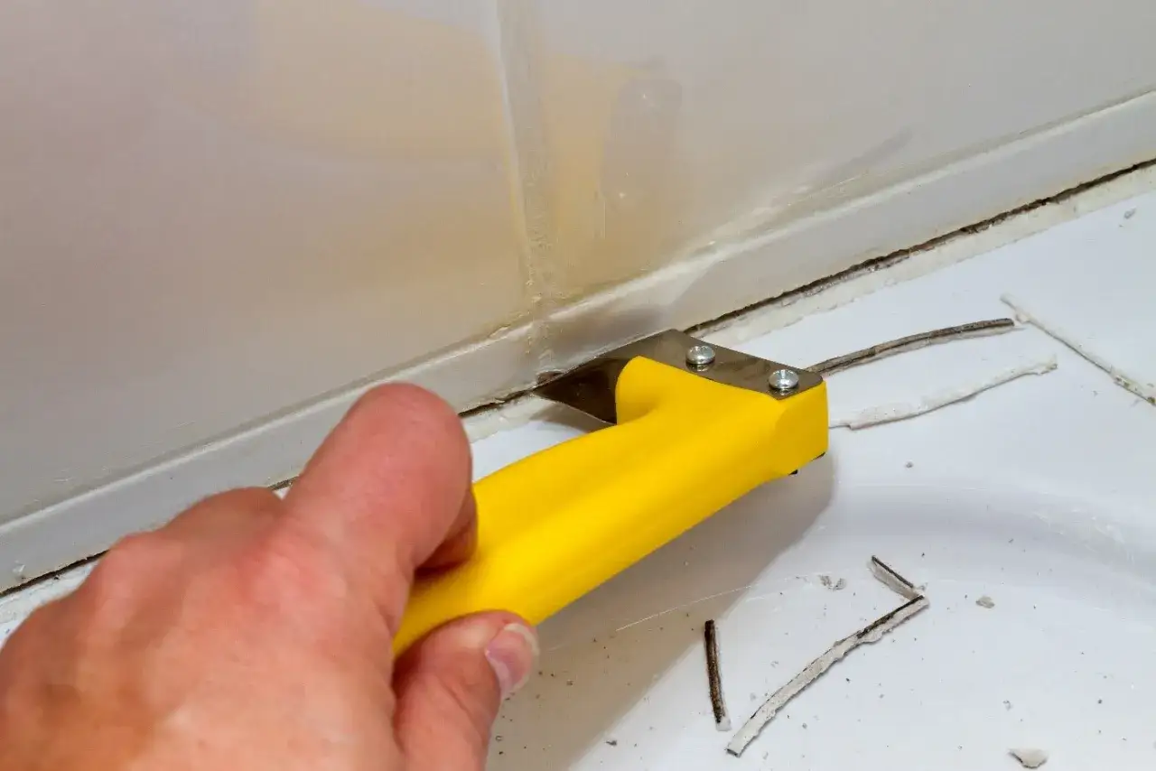 Main jaune pour refaire joint douche. L'outil retire l'ancien joint abîmé.