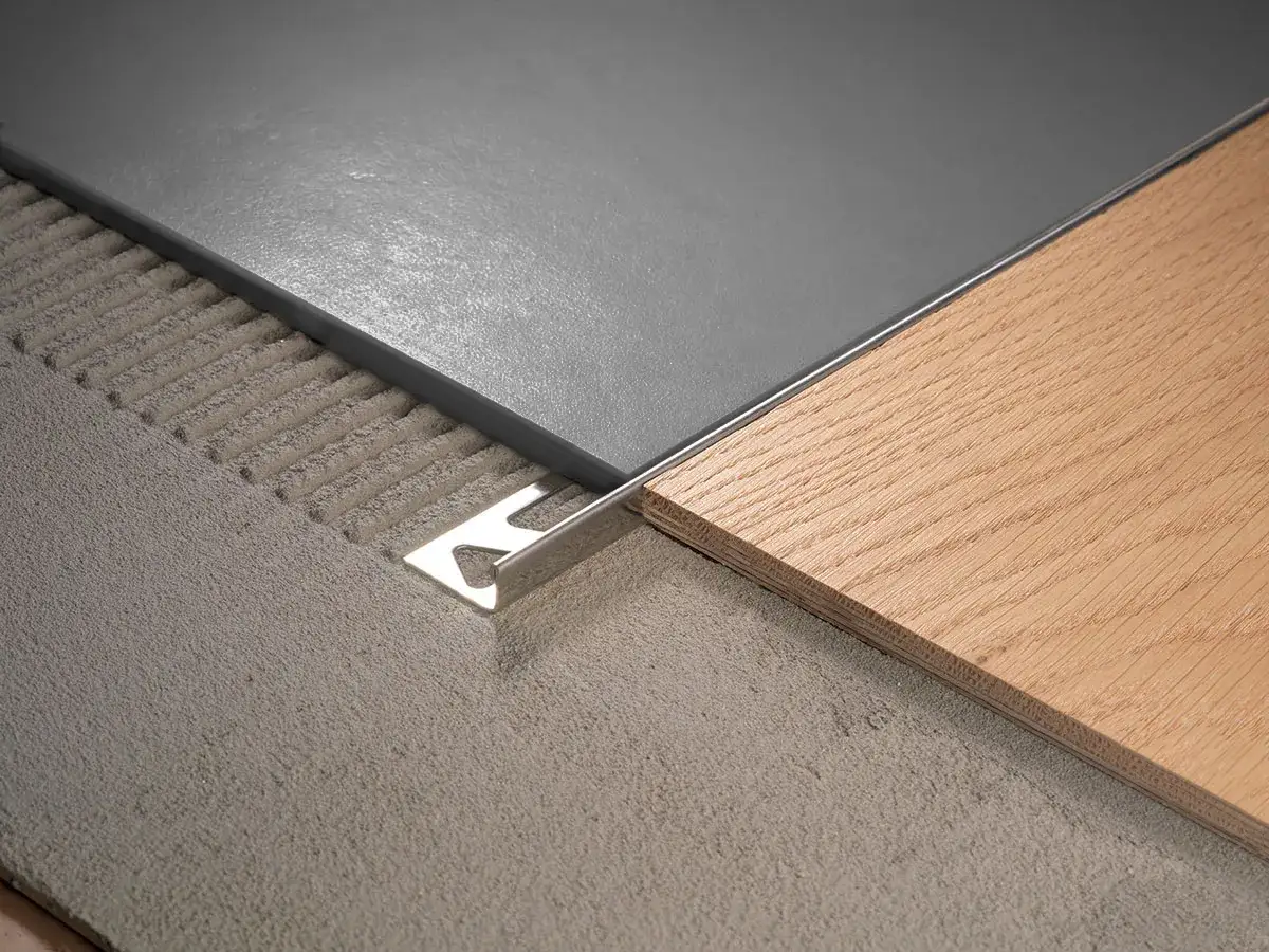 Détail d'une barre de seuil entre carrelage gris et parquet en bois clair, posée sur un lit de mortier.