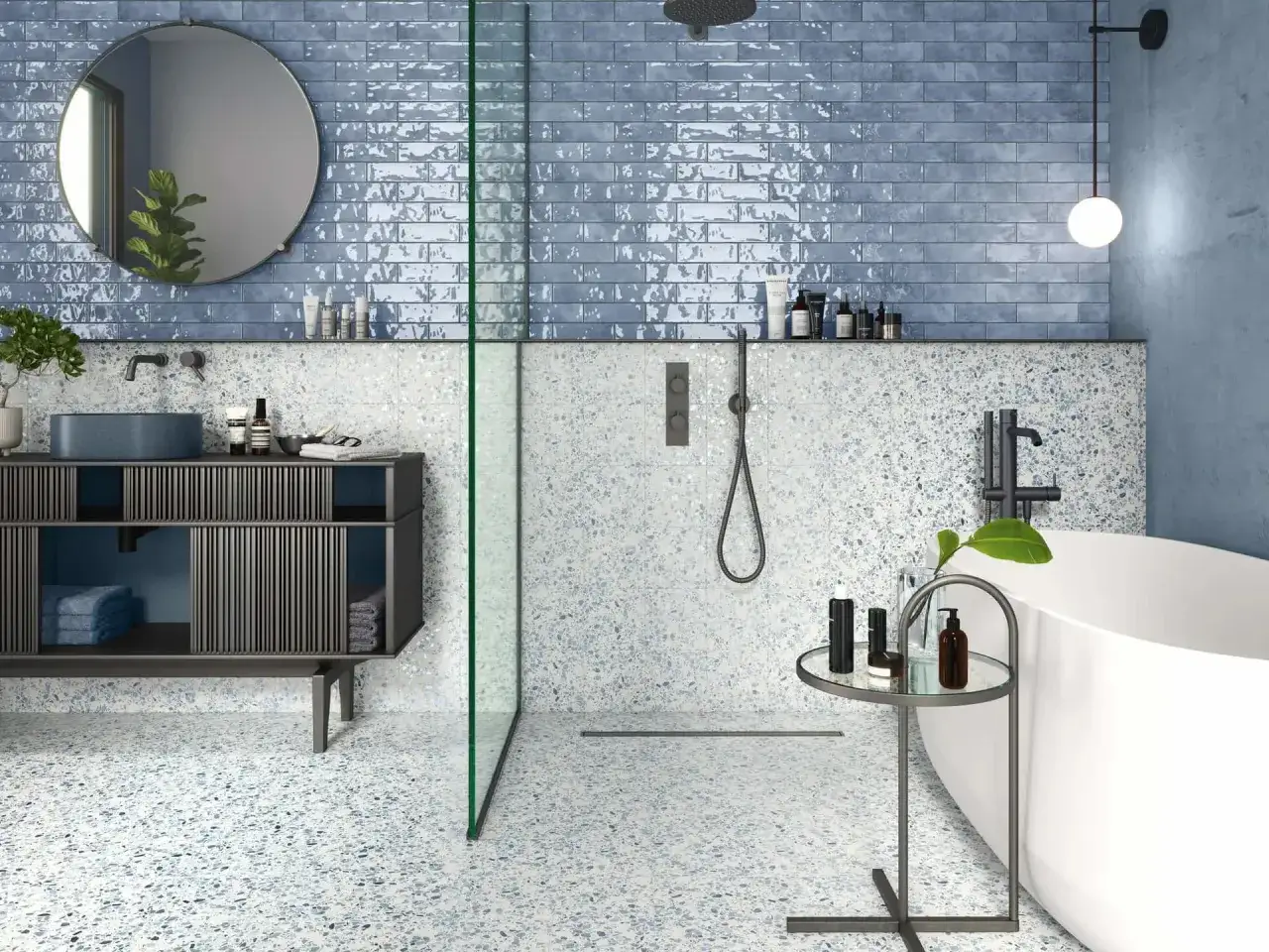 Salle de bain moderne avec murs en faïence bleue brillante et sol en terrazzo. Douche vitrée, baignoire, meuble vasque et miroir rond.