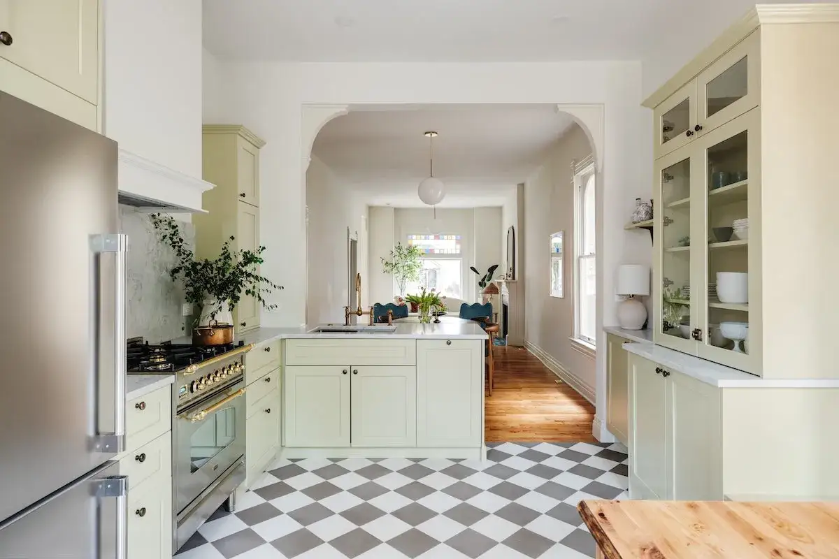 Cuisine lumineuse avec des armoires vert pâle, un îlot central et un sol à carreaux de ciment gris et blancs.