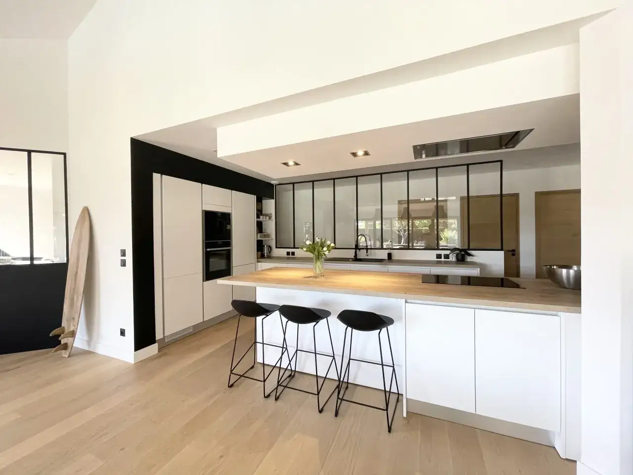 Moderne cuisine ouverte avec îlot central, tabourets noirs et plan de travail en bois. Un style épuré et lumineux.